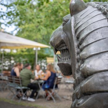 Ein Löwestatue im Vordergrund, mit Biergarten im Hintergrund